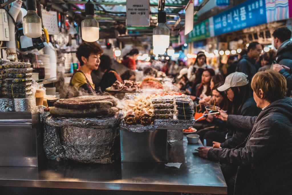 A bustling street market in Seoul, South Korea, with a focus on a food stall