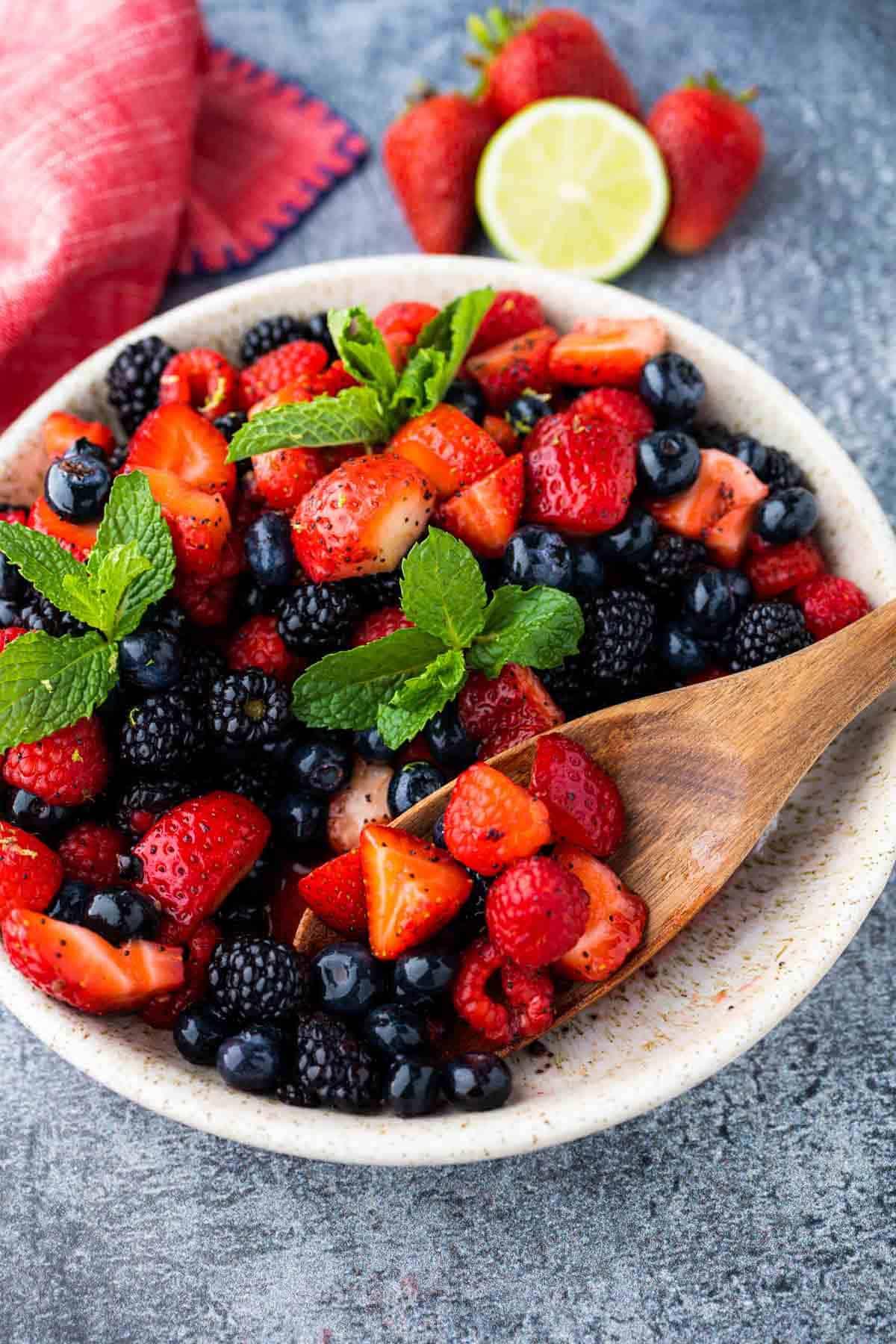 A vibrant mixed berry salad with a honey-lime dressing being poured over the top
