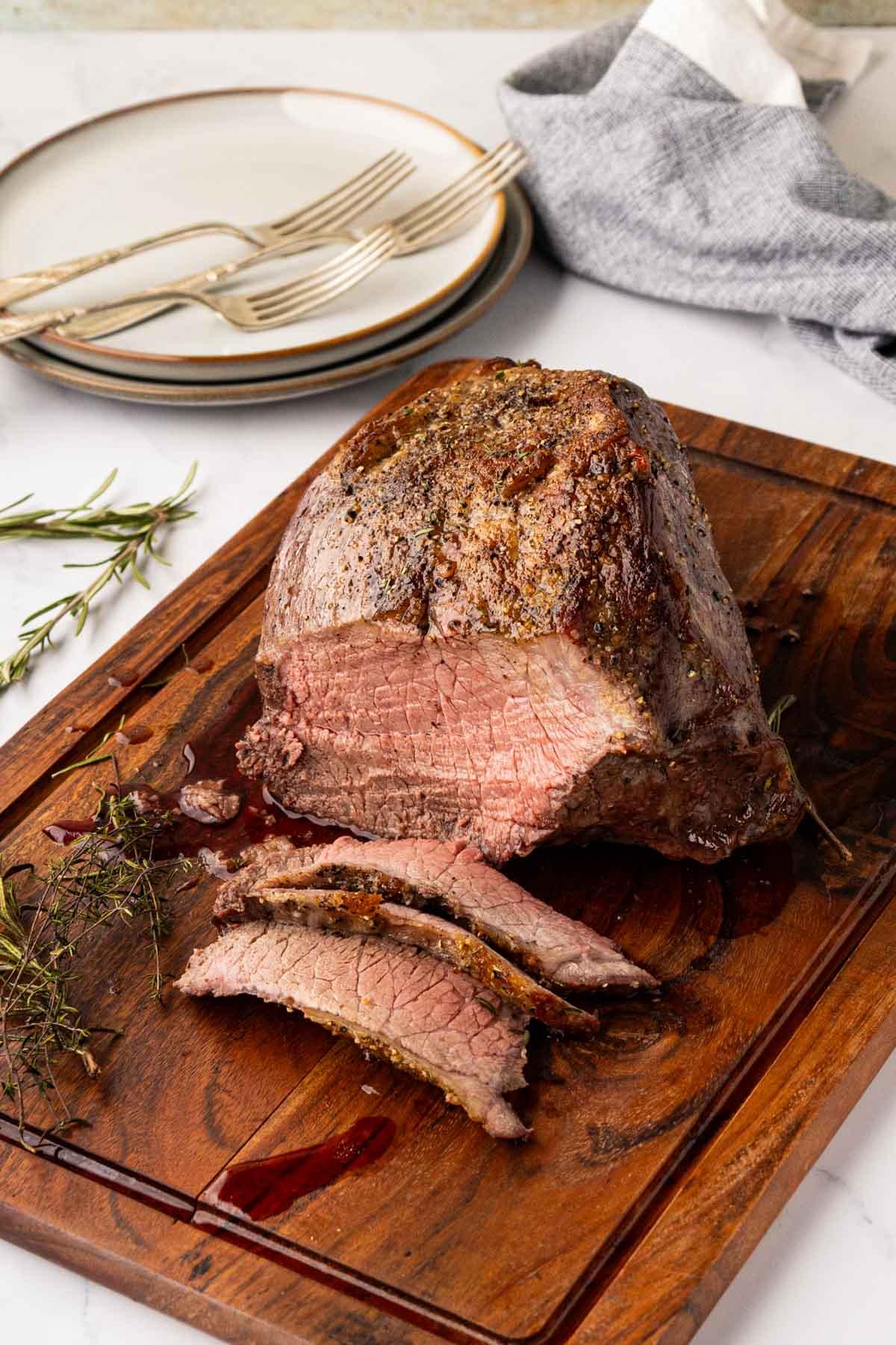 sliced, perfectly cooked garlic butter roast beef with juices visible, on a cutting board