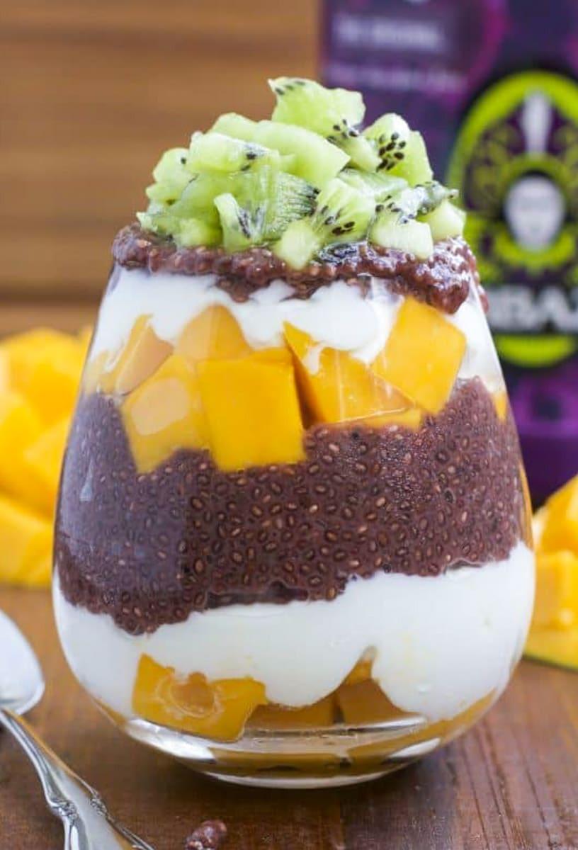 Close-up shot of a glass filled with layers of mango chia pudding, granola, and fresh mango slices