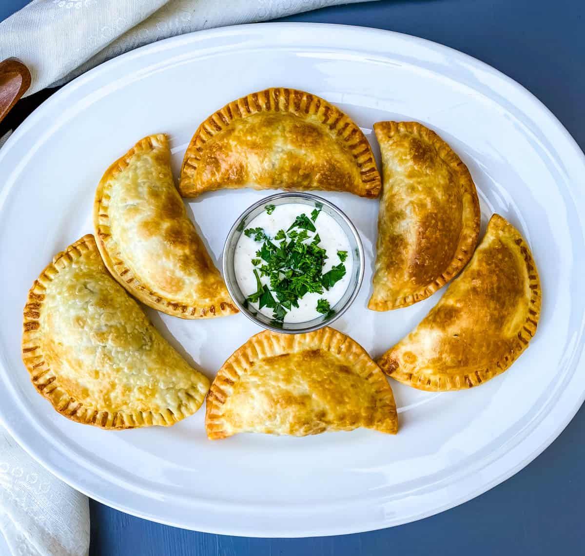 A table laden with freshly grilled vegetable empanadas, surrounded by people enjoying them.
