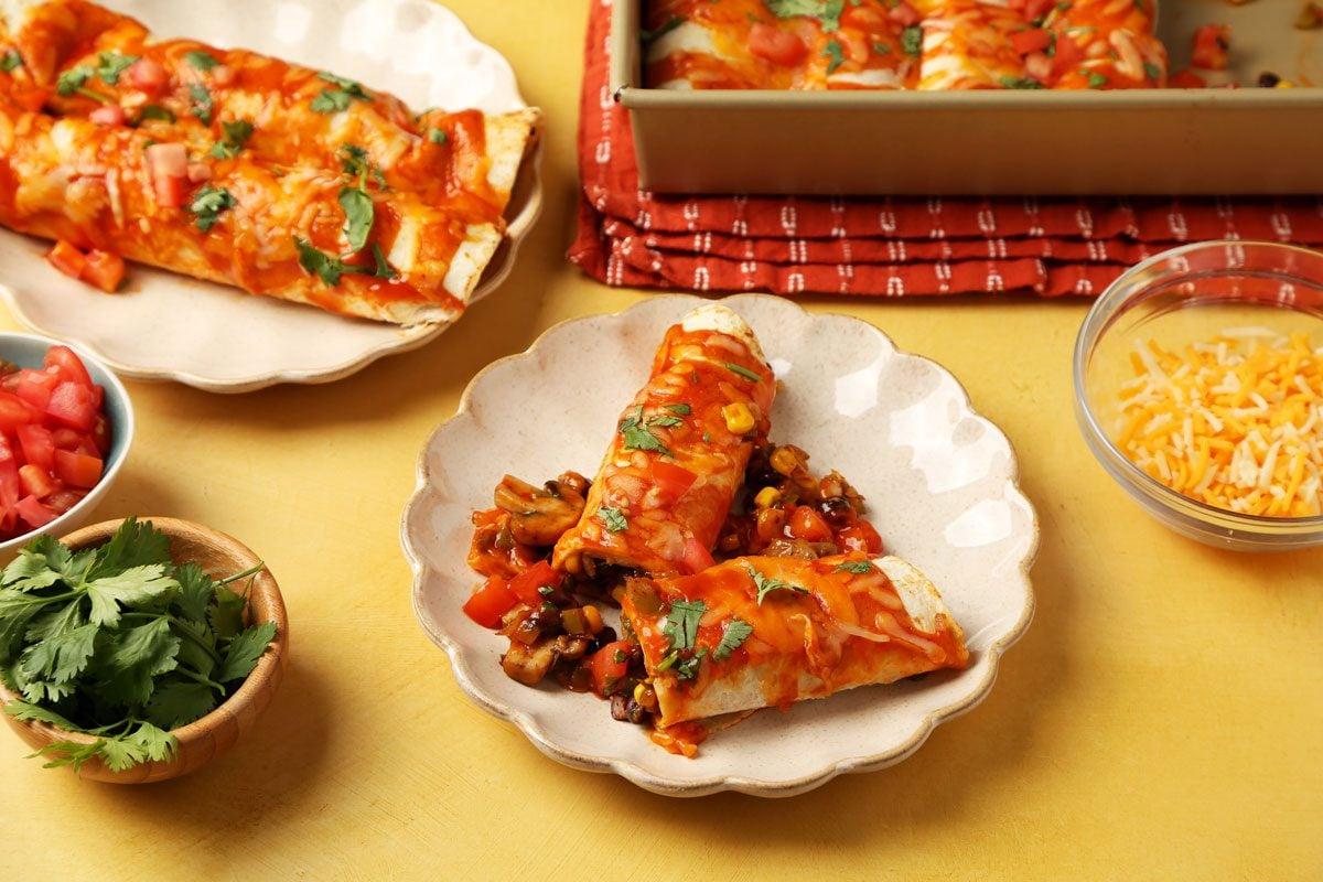 A table setting with a plate of cashew cheese enchiladas, garnished with fresh cilantro and red onion.