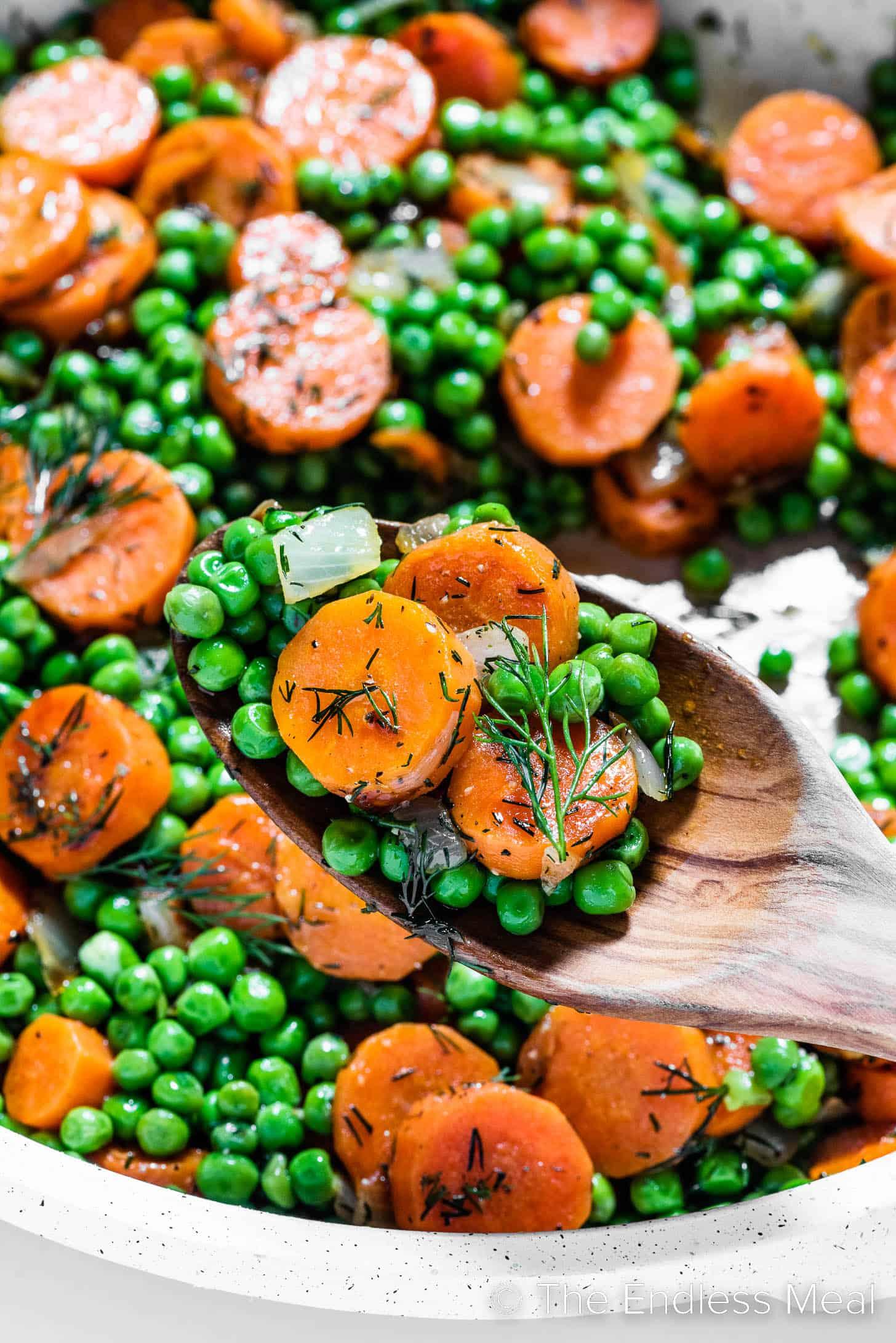 A close-up of the peas and carrots in the skillet during cooking, showing their vibrant colors.