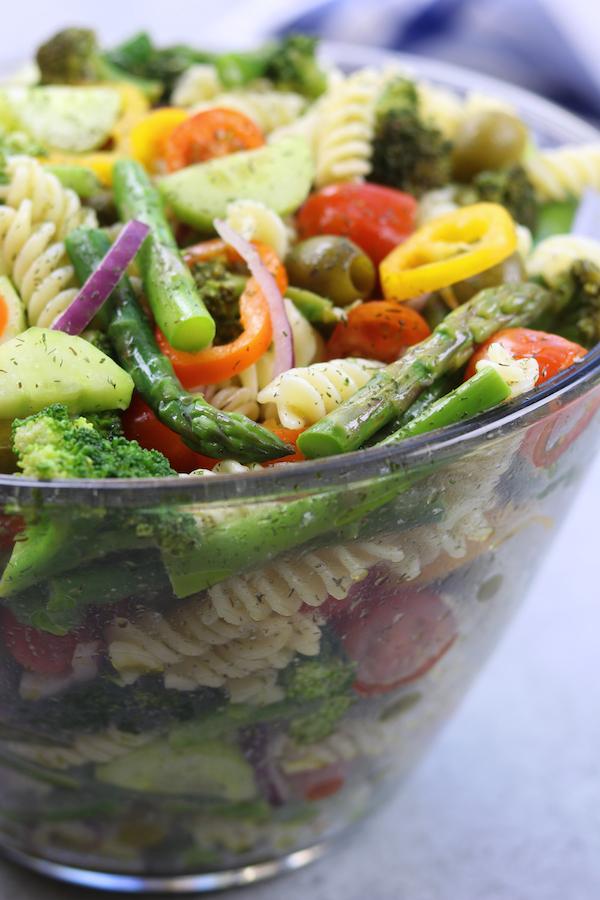 A person tossing a large bowl of Springtime Garden Pasta Salad.