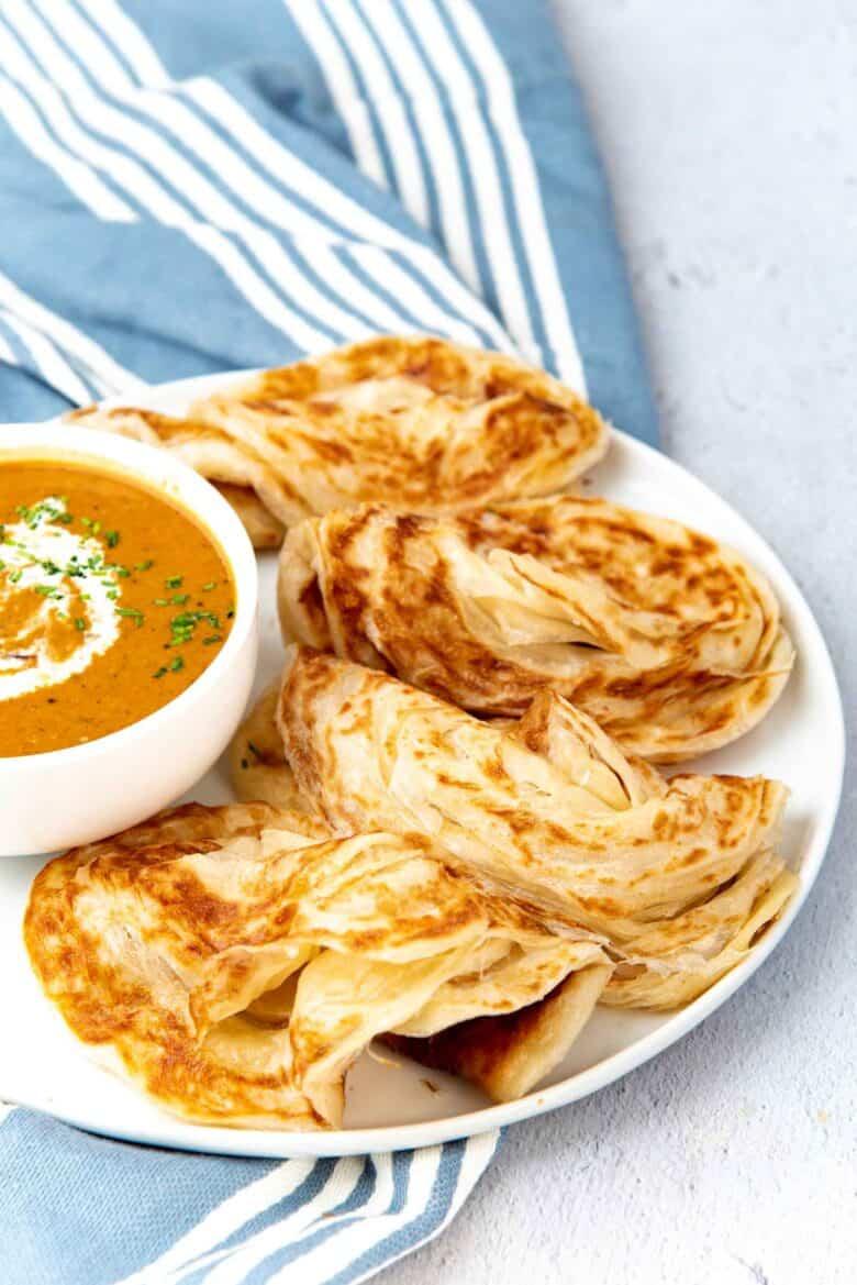 Close up shot of golden brown roti on a plate with a side of curry