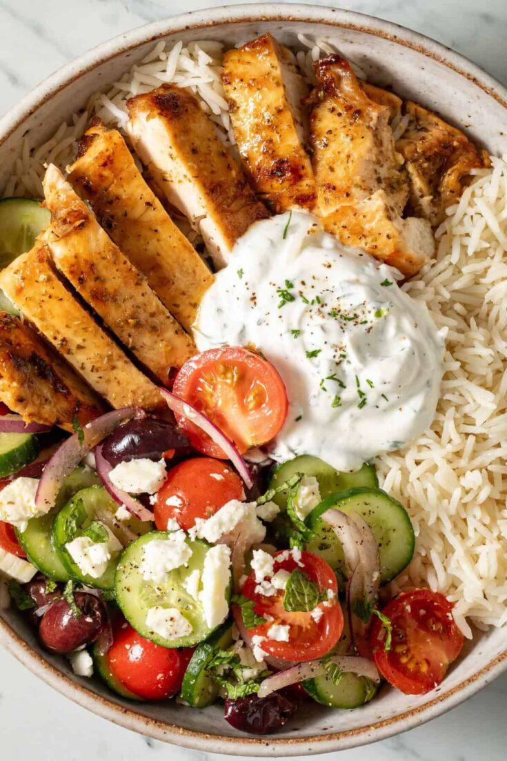Overhead shot of two women sharing a vibrant Greek chicken bowl at a sunny outdoor cafe in Crete