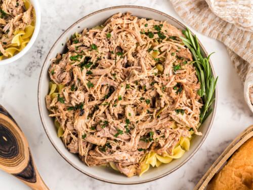 Close-up shot of a bowl of gluten-free pasta tossed with tender pulled pork, showing the texture and color of the dish
