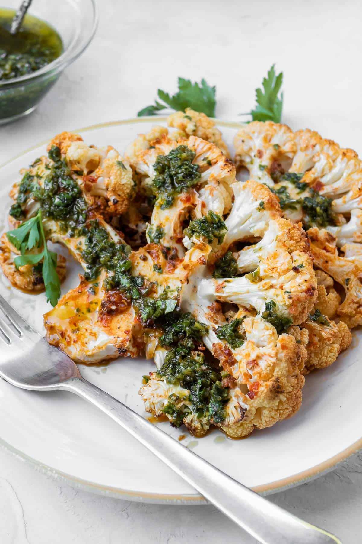 Close-up shot of perfectly roasted Mediterranean-style cauliflower steaks, seasoned and glistening, on a rustic wooden board.