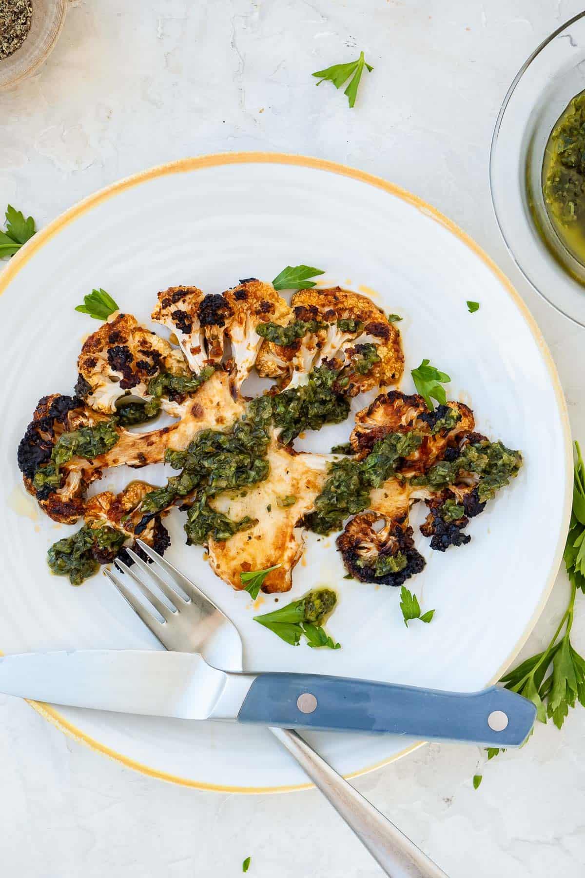 A beautifully styled table setting with a plate of Mediterranean-Style Roasted Cauliflower Steaks as the centerpiece.