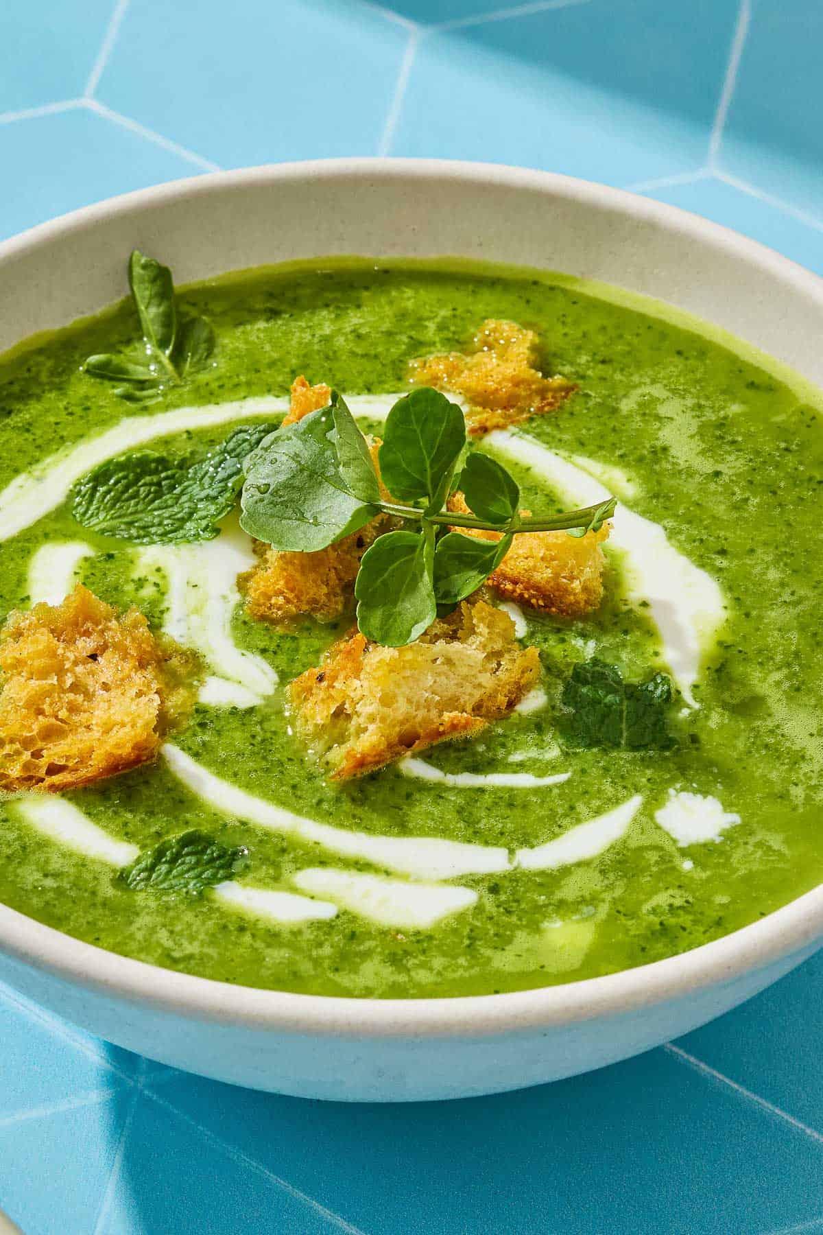 hands ladling callaloo and watercress soup into a rustic bowl, garnished with fresh herbs