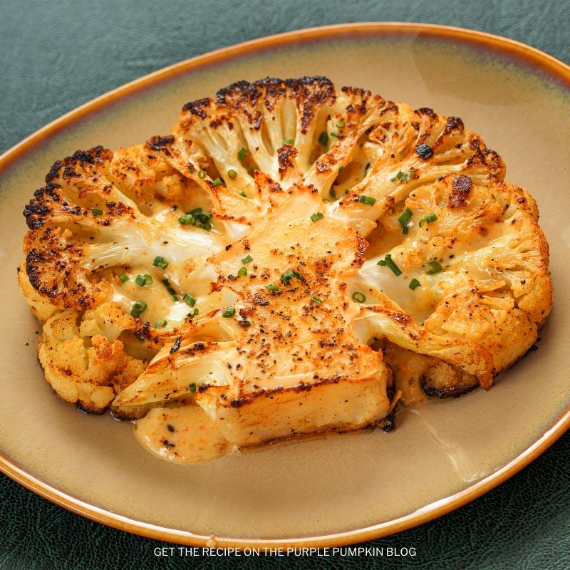 Close-up shot of herb-crusted cauliflower steaks with parmesan cheese, drizzled with olive oil, on a rustic wooden cutting board.