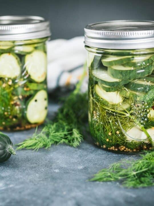 A rustic wooden table with a bowl of bright green cucumber-dill tzatziki, surrounded by fresh cucumbers, dill sprigs, and a lemon wedge