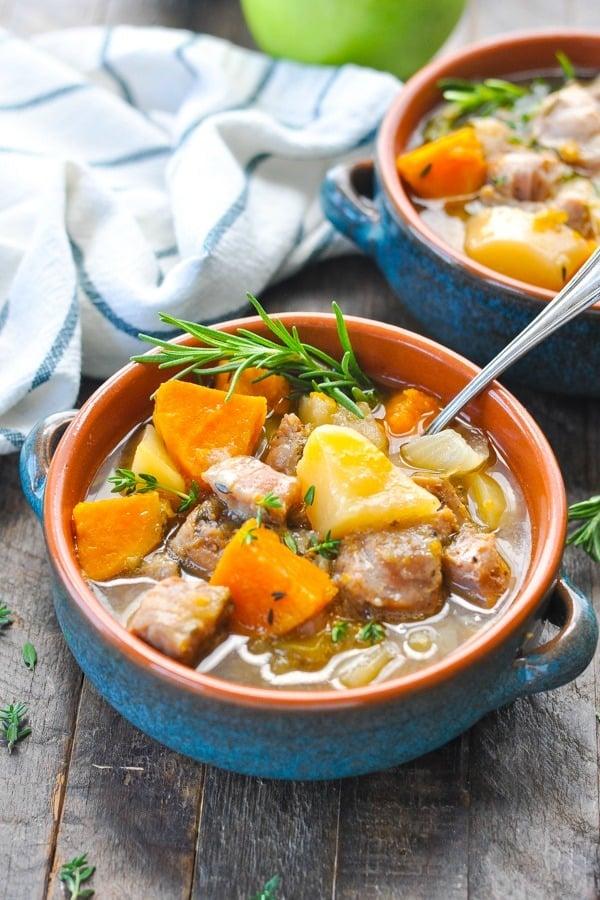 A rustic autumnal scene of a hearty pork stew with apples and cider simmering in a Dutch oven