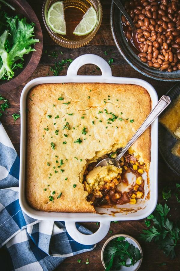 A rustic wooden table with a large casserole dish of Pulled Pork Mac and Cheese and a separate bowl of coleslaw.