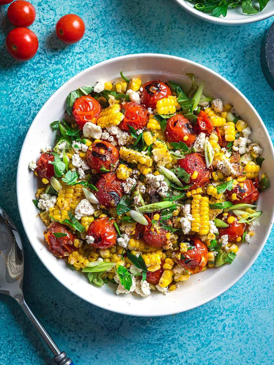 overhead shot of freshly grilled corn and blistered cherry tomatoes on a rustic wooden table