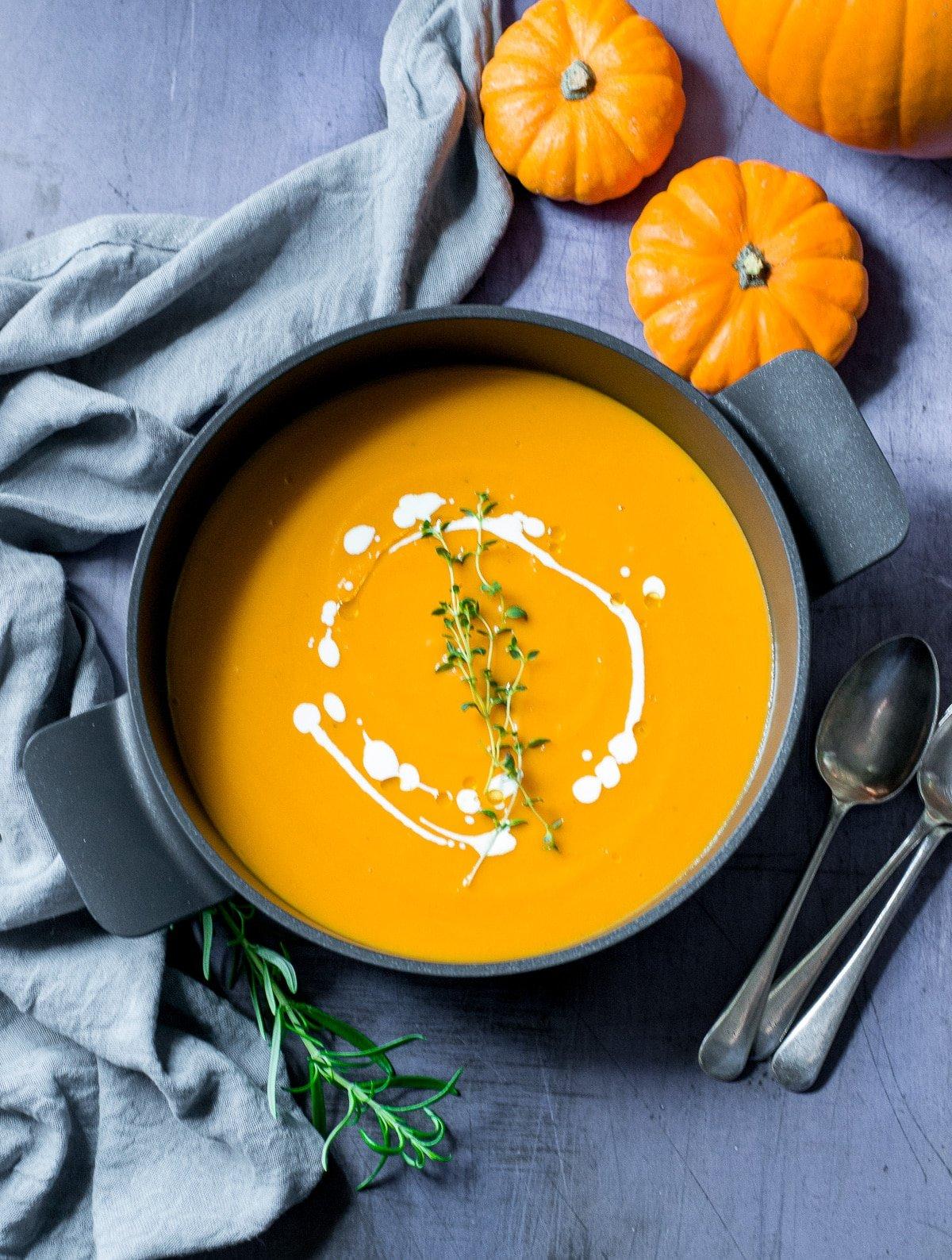 Close-up shot of a steaming bowl of pumpkin soup, garnished with toasted pecans and a sprig of rosemary.