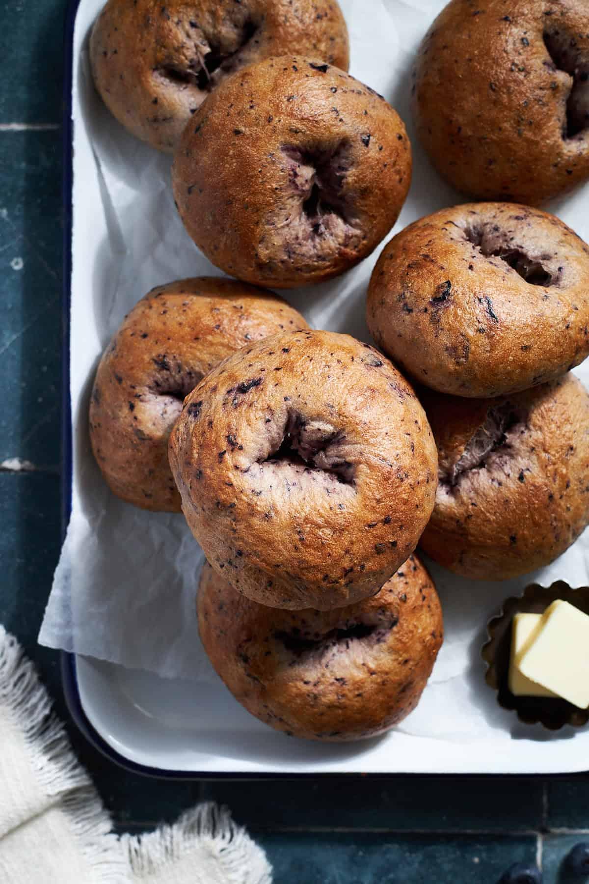 Hands reaching for blueberry bagel bites on a wooden board, with a cup of coffee in the background