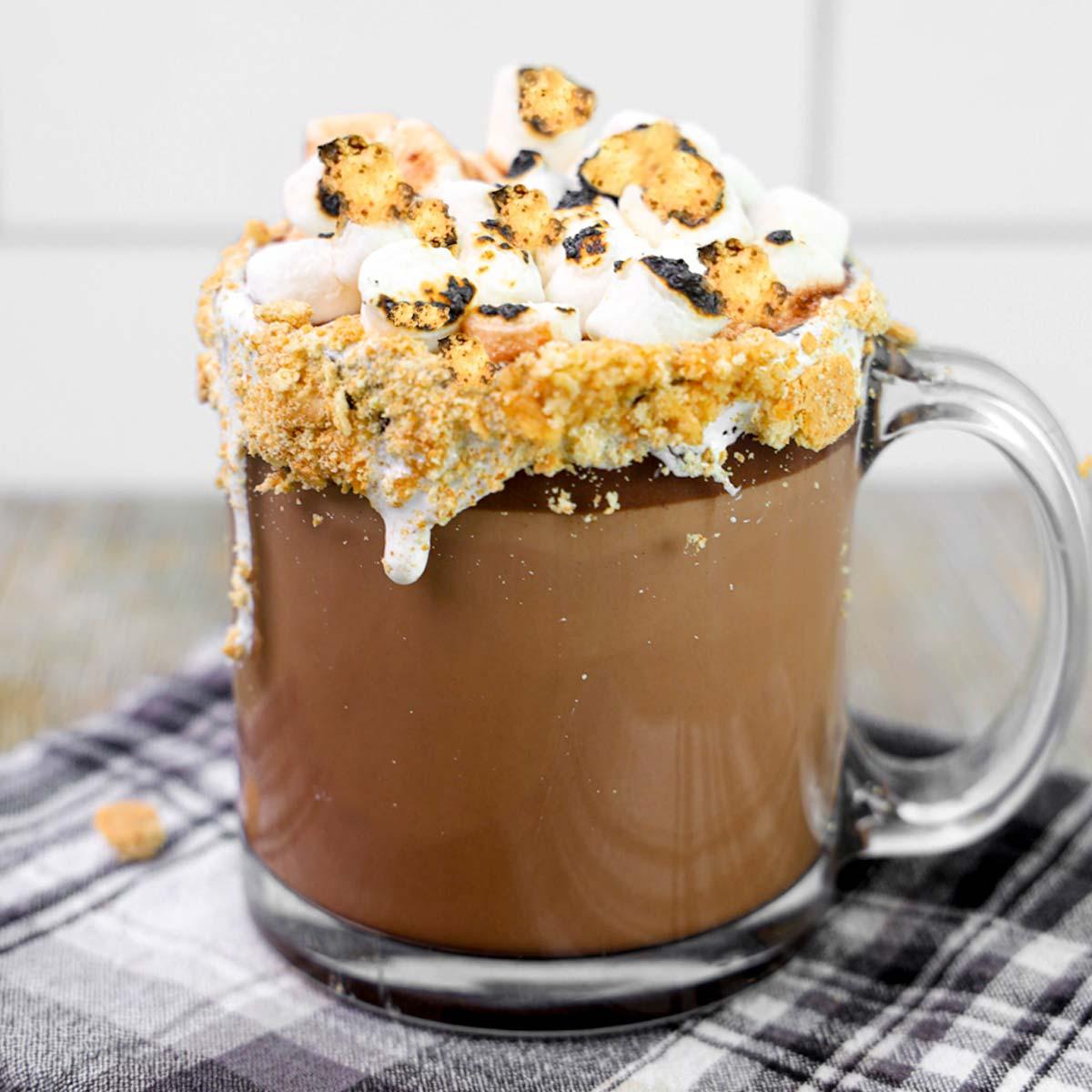 Overhead shot of several mugs of S'mores Campfire Delight Hot Chocolate, garnished with graham crackers and chocolate shavings