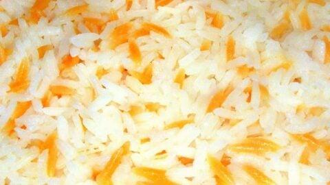 A close-up shot of a bowl of fluffy steamed rice next to a colorful serving of Turkish pilav