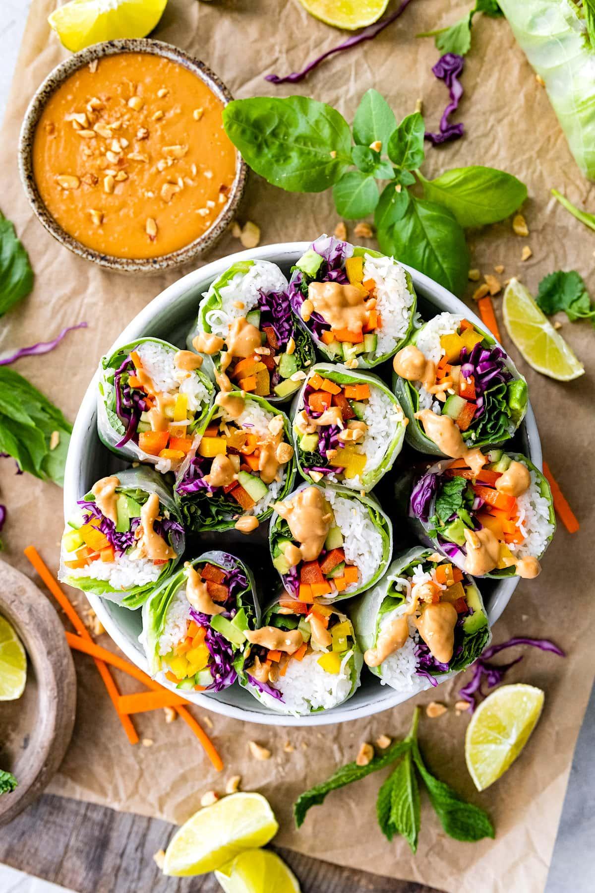 A platter of Plantain Spring Rolls arranged artfully, drizzled with peanut sauce and garnished with fresh herbs.