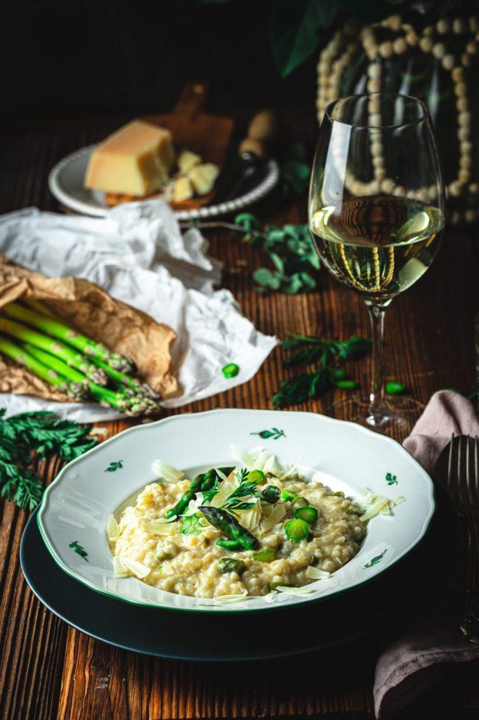 A glass of white wine next to a pot of cooking Spring Asparagus and Green Bean Risotto