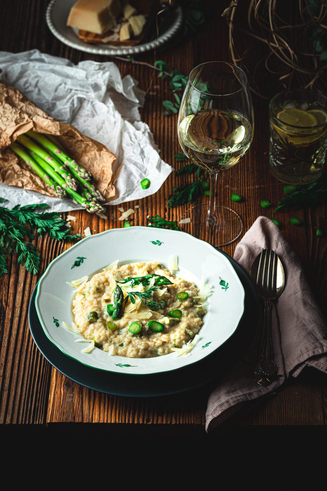 A rustic wooden table set with a bowl of creamy asparagus risotto, garnished with fresh rosemary sprigs