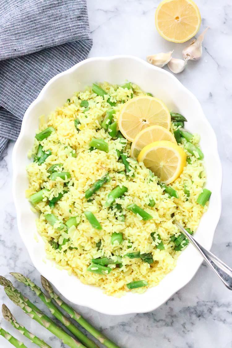A bowl of fluffy steamed rice topped with bright green steamed asparagus spears and a squeeze of lemon juice.