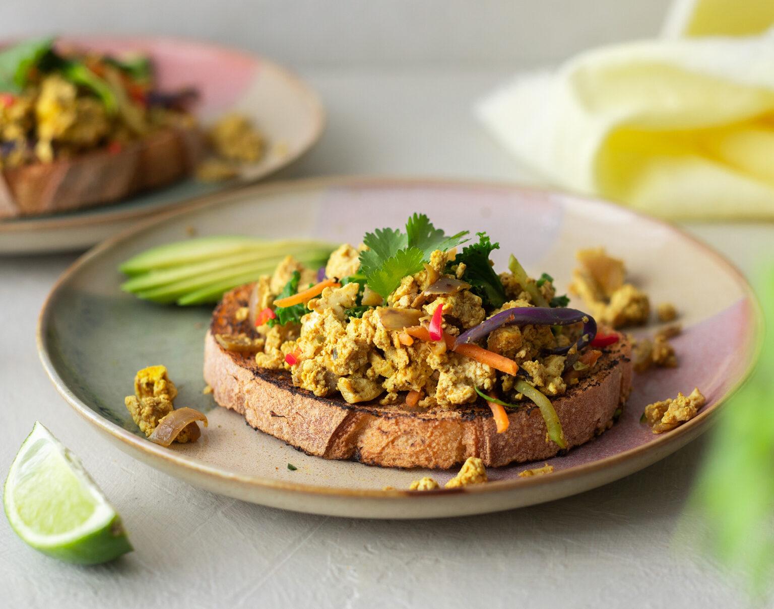 Finished black truffle tofu scramble with arugula served on a plate with a side of toasted bread