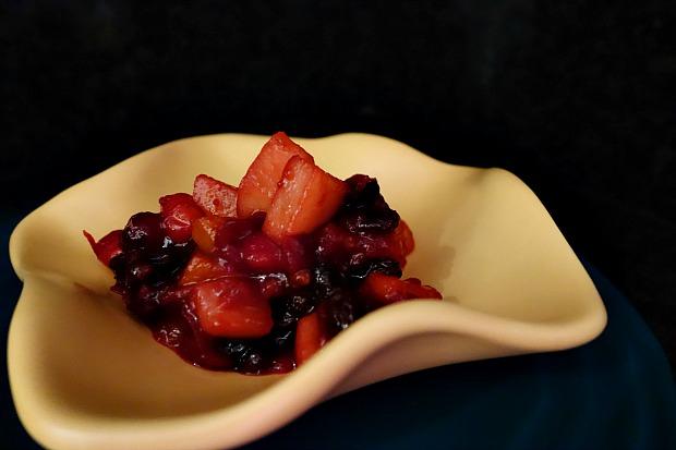 Hands gently stirring a pot of Thanksgiving fruit compote, a warm and inviting kitchen in the background.