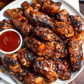 A plate of grilled bourbon bbq chicken wings with dipping sauces
