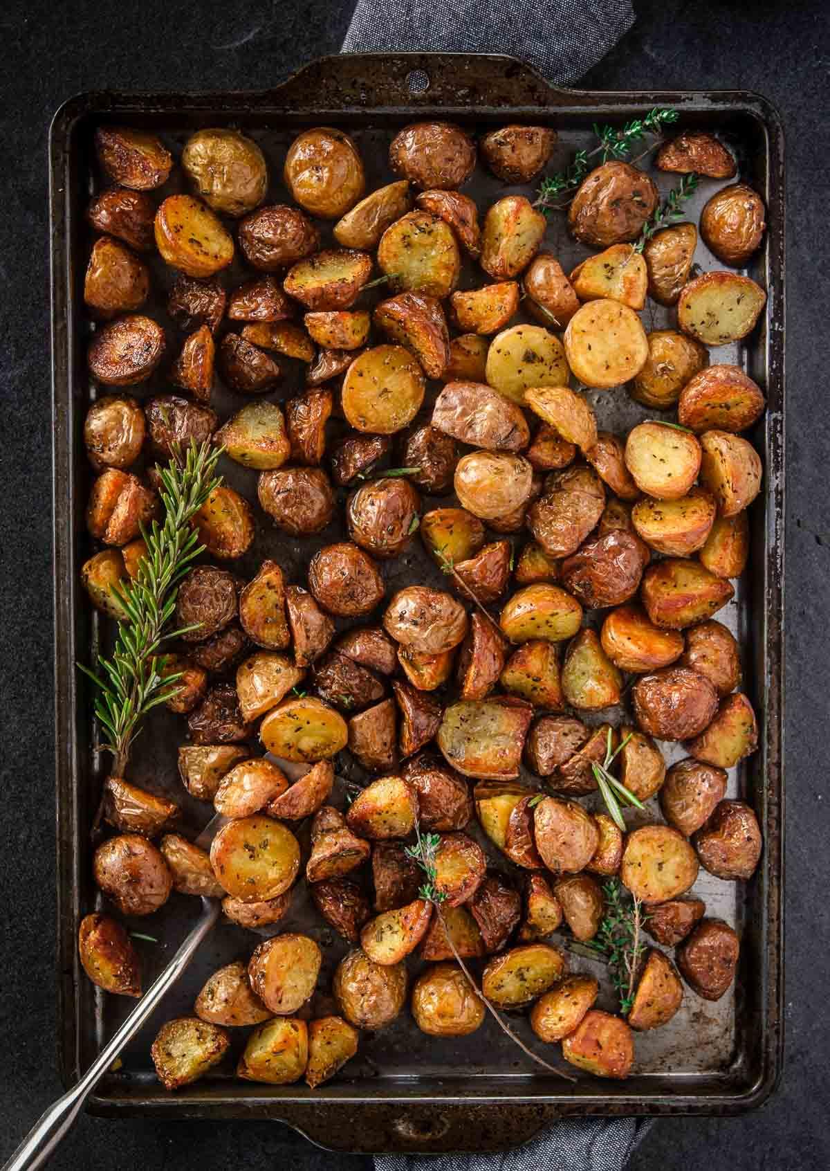 A rustic kitchen setting with a baking sheet of roasted potatoes in the foreground.
