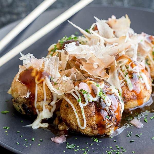 Golden-brown takoyaki balls on a plate, garnished with bonito flakes, takoyaki sauce, mayonnaise, and green onions