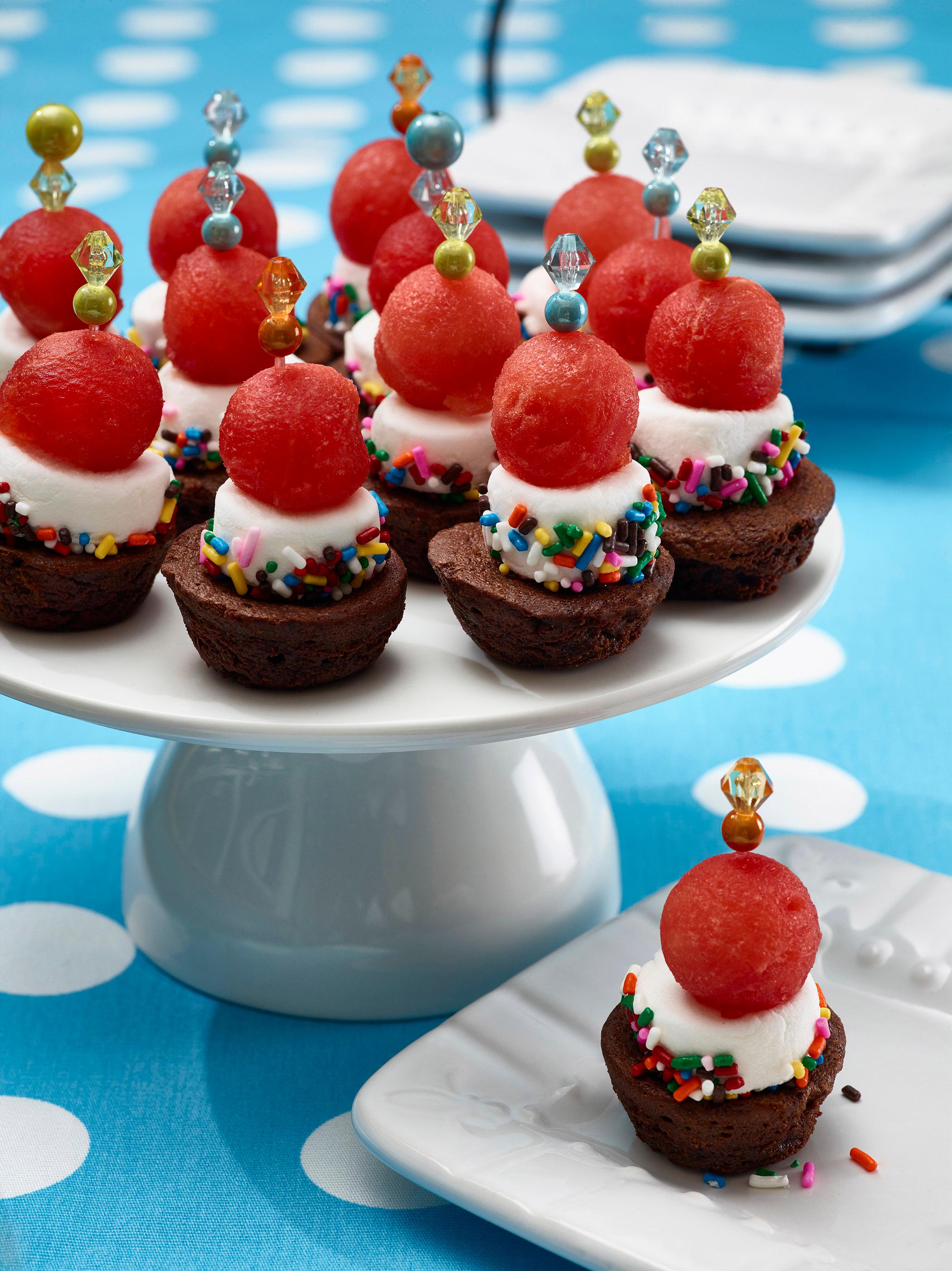 A person serving a plate of brownie bites to a group of friends.