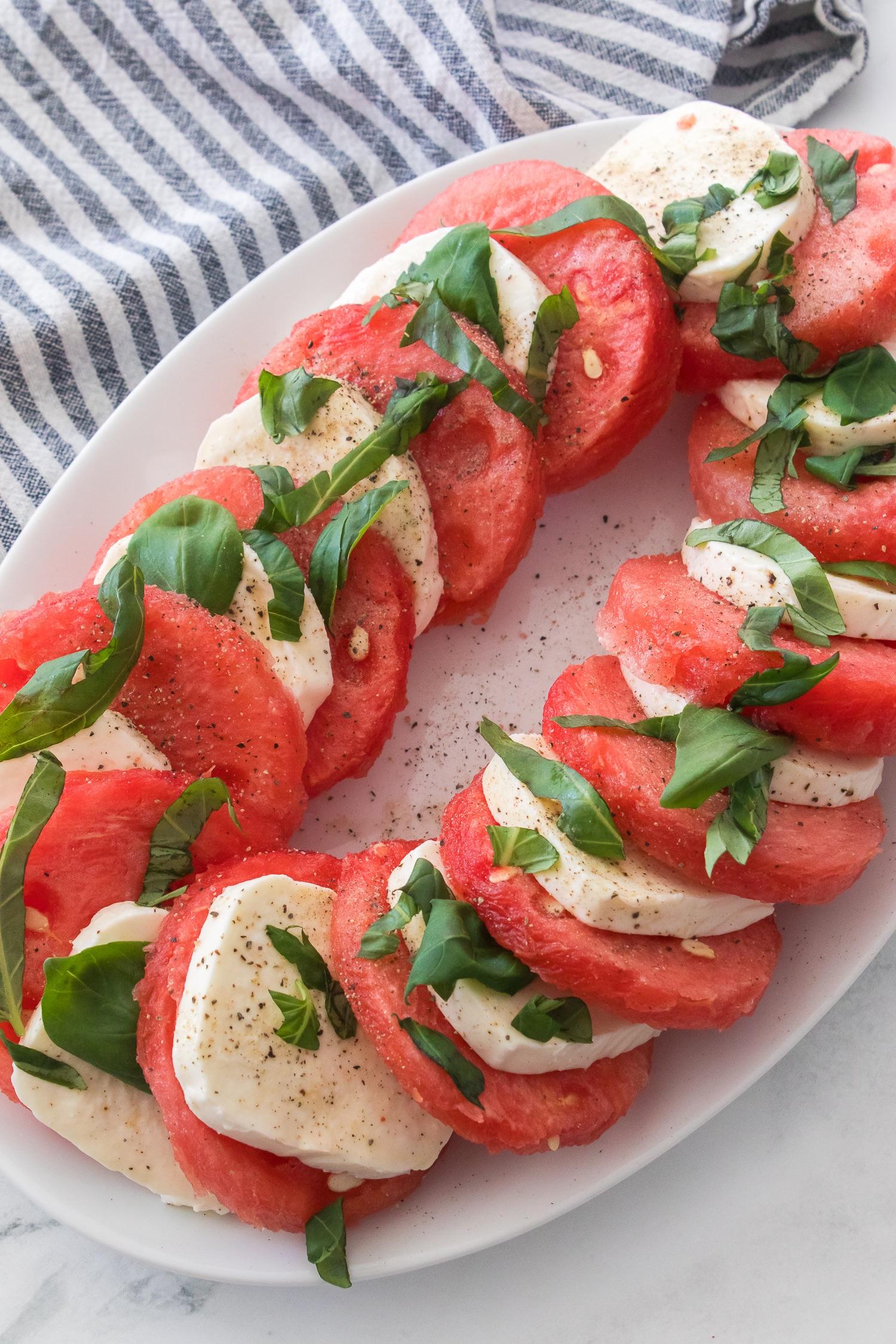 A beautifully styled watermelon and mozzarella salad served on a rustic wooden platter, garnished with fresh basil leaves.