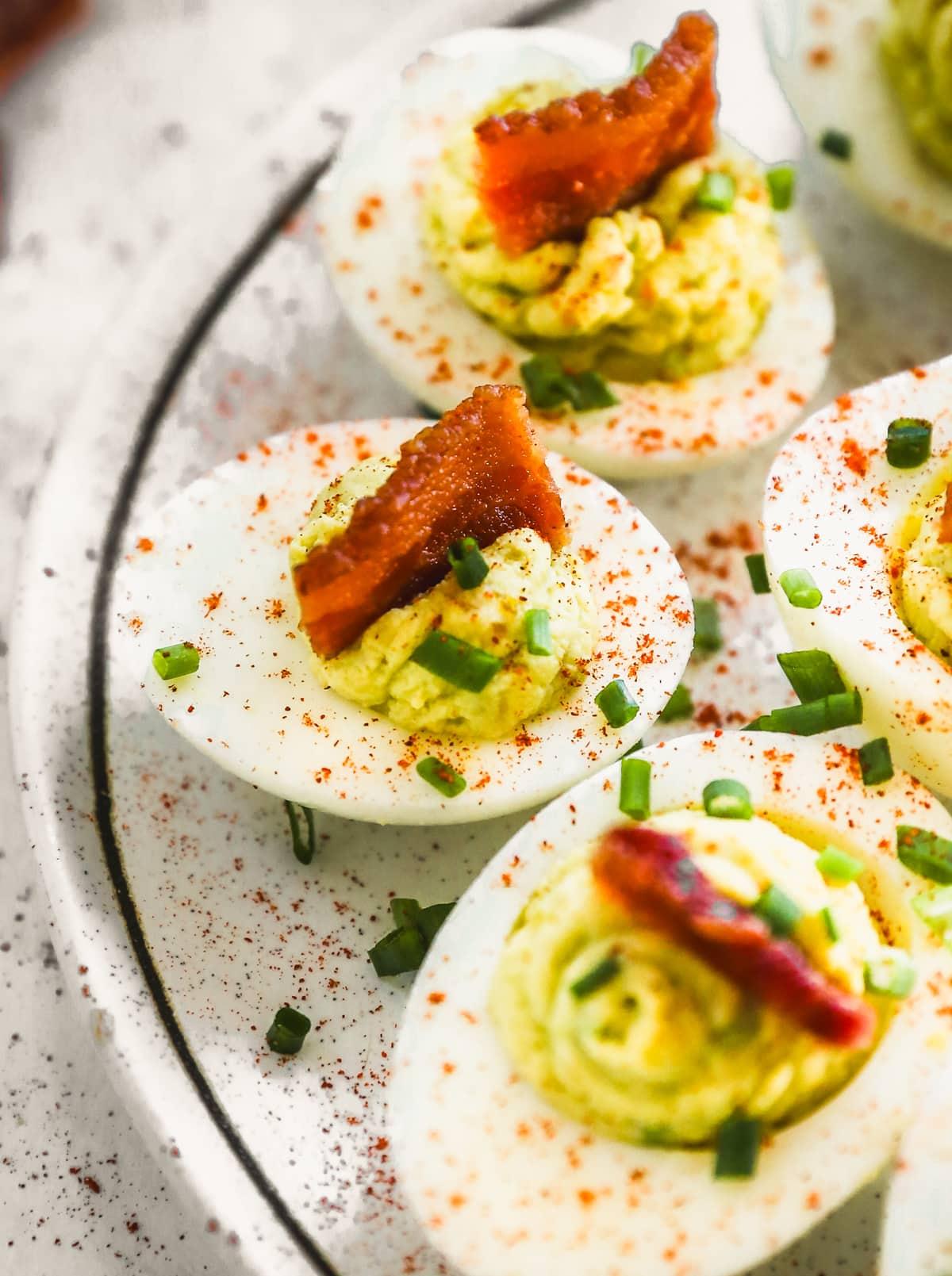 Close-up shot of creamy avocado ranch deviled eggs on a white plate garnished with fresh herbs