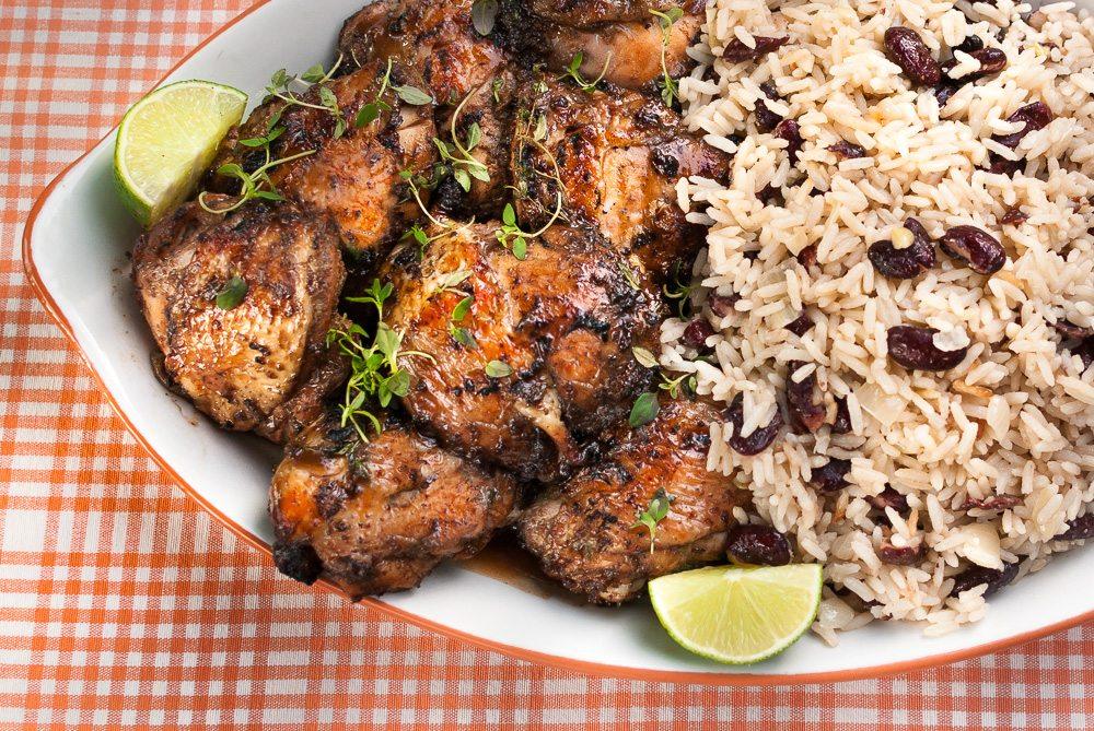 A steaming plate of jerk chicken with rice and peas