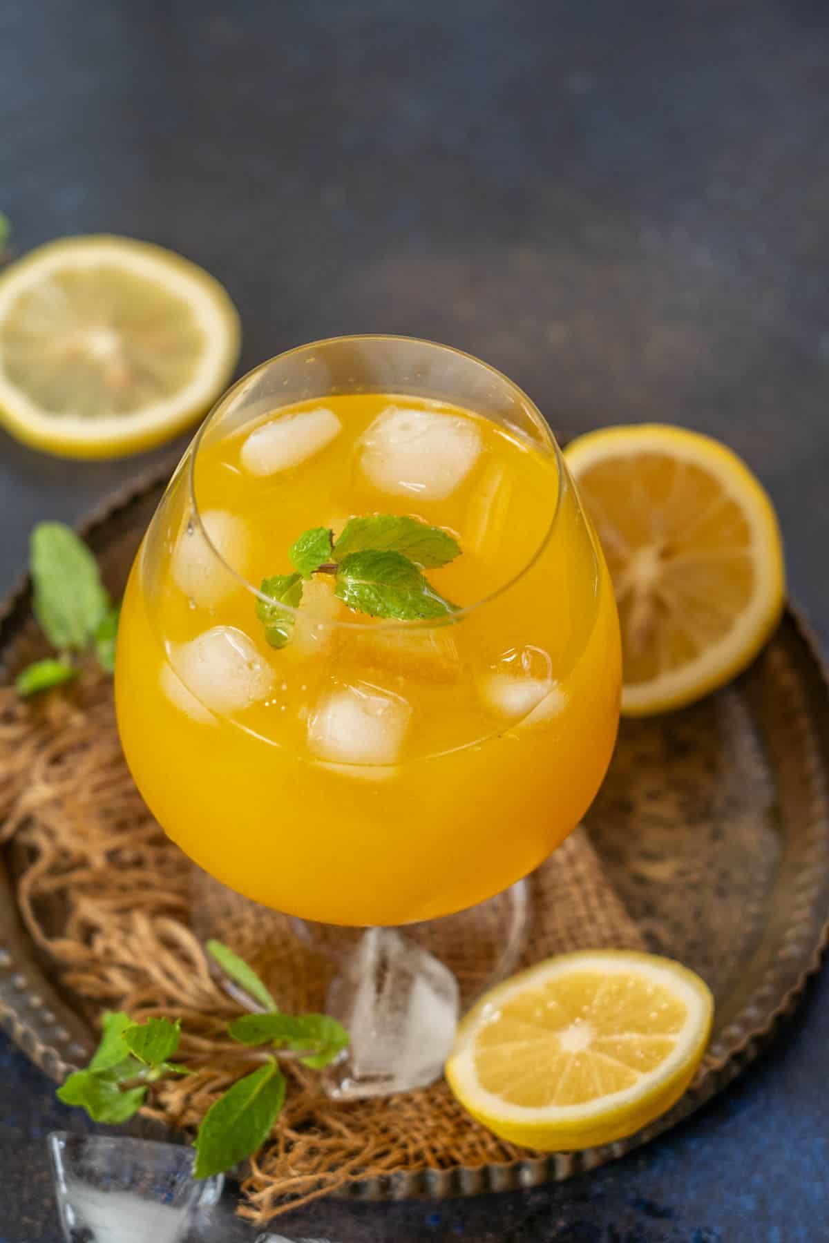 Glass of golden yellow lemonade with visible slices of ginger and lemon, garnished with a turmeric strip