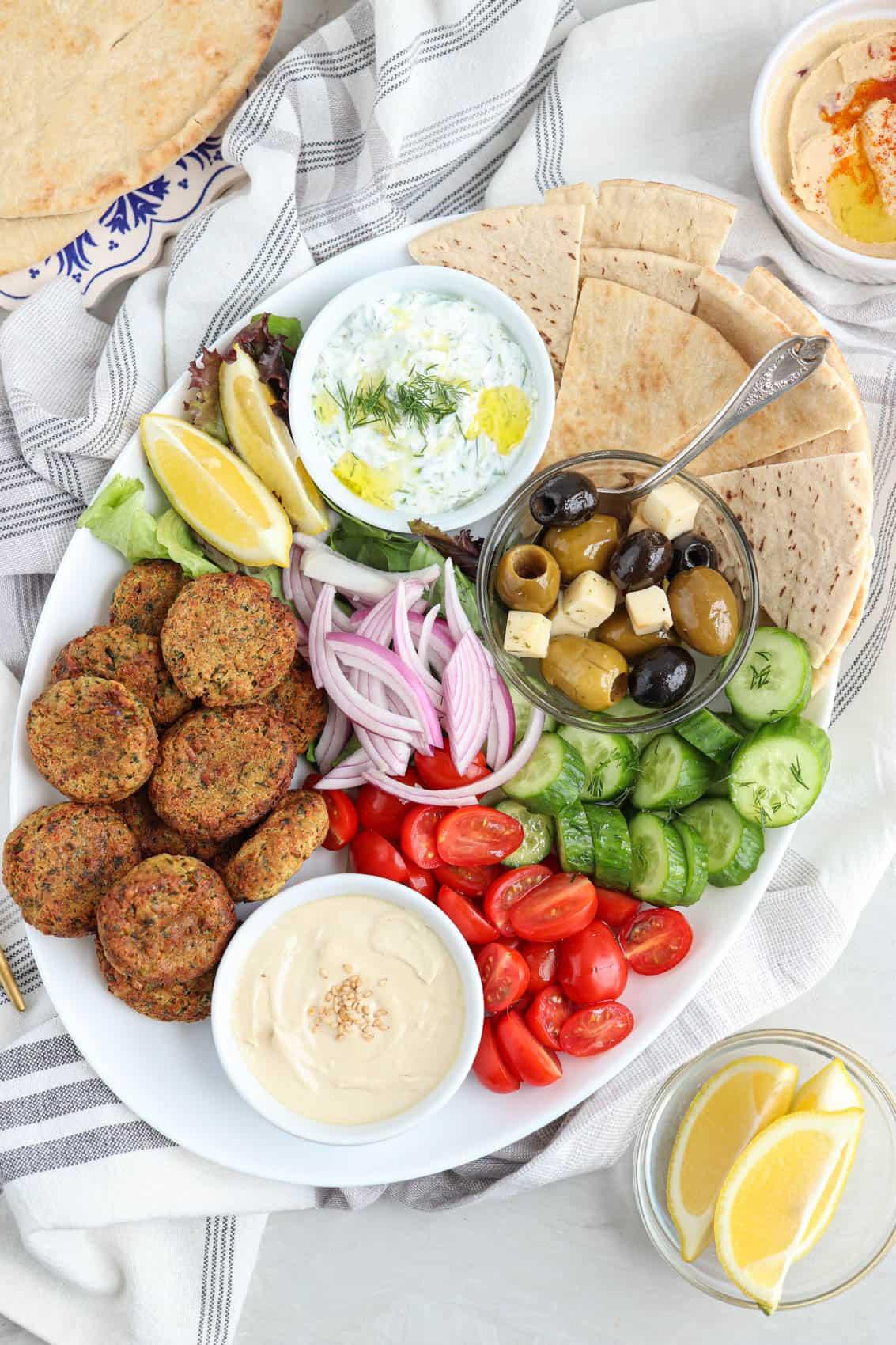 A table with falafel, pita bread, hummus, and various other mezze dishes