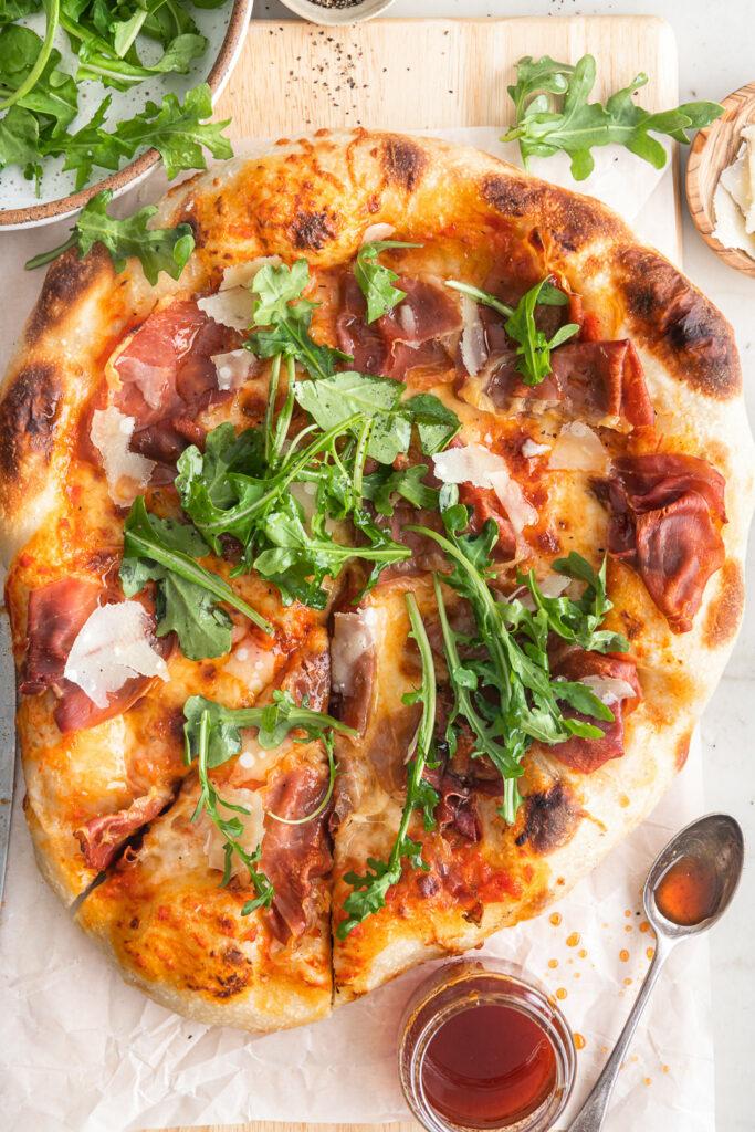 Close-up shot of a delicious curry pizza with prosciutto and arugula