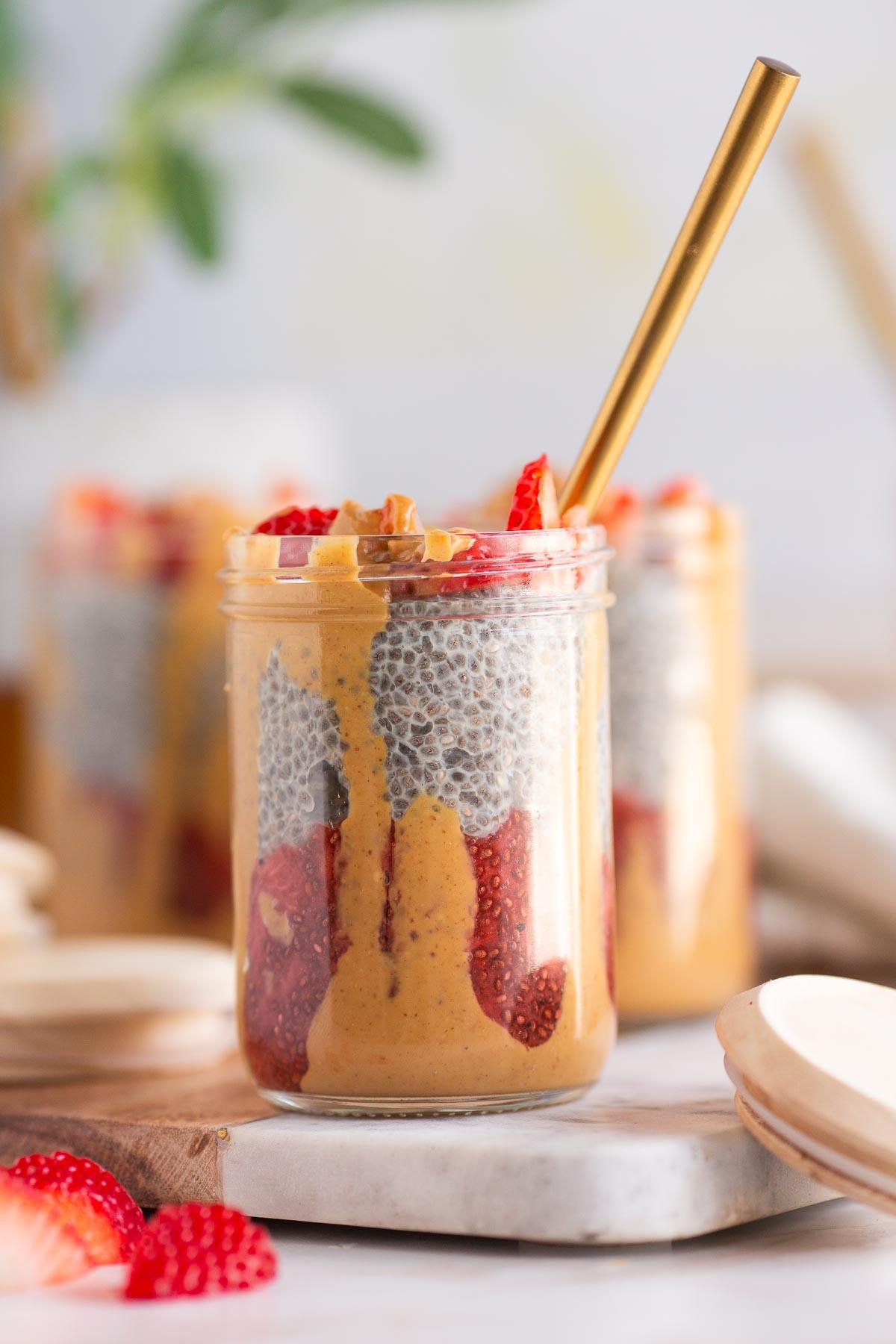 A rustic wooden table with a glass jar of peanut butter cup chia pudding, along with a spoon and fresh berries