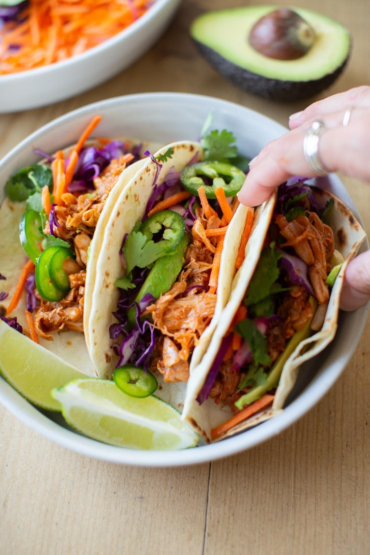 a person holding a plate of chimichurri jackfruit tacos