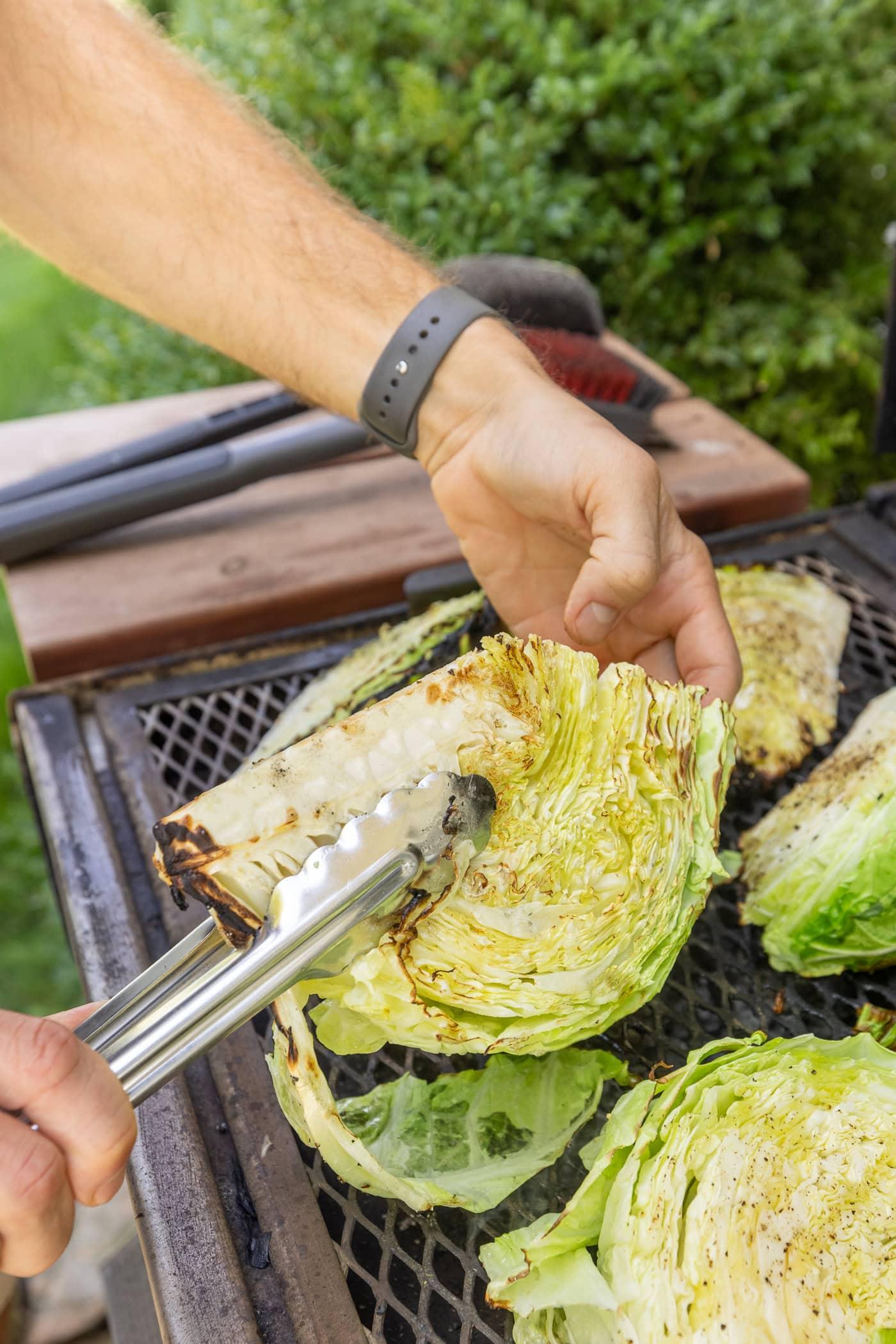 A person serving a grilled vegetable and cabbage salad at an outdoor gathering