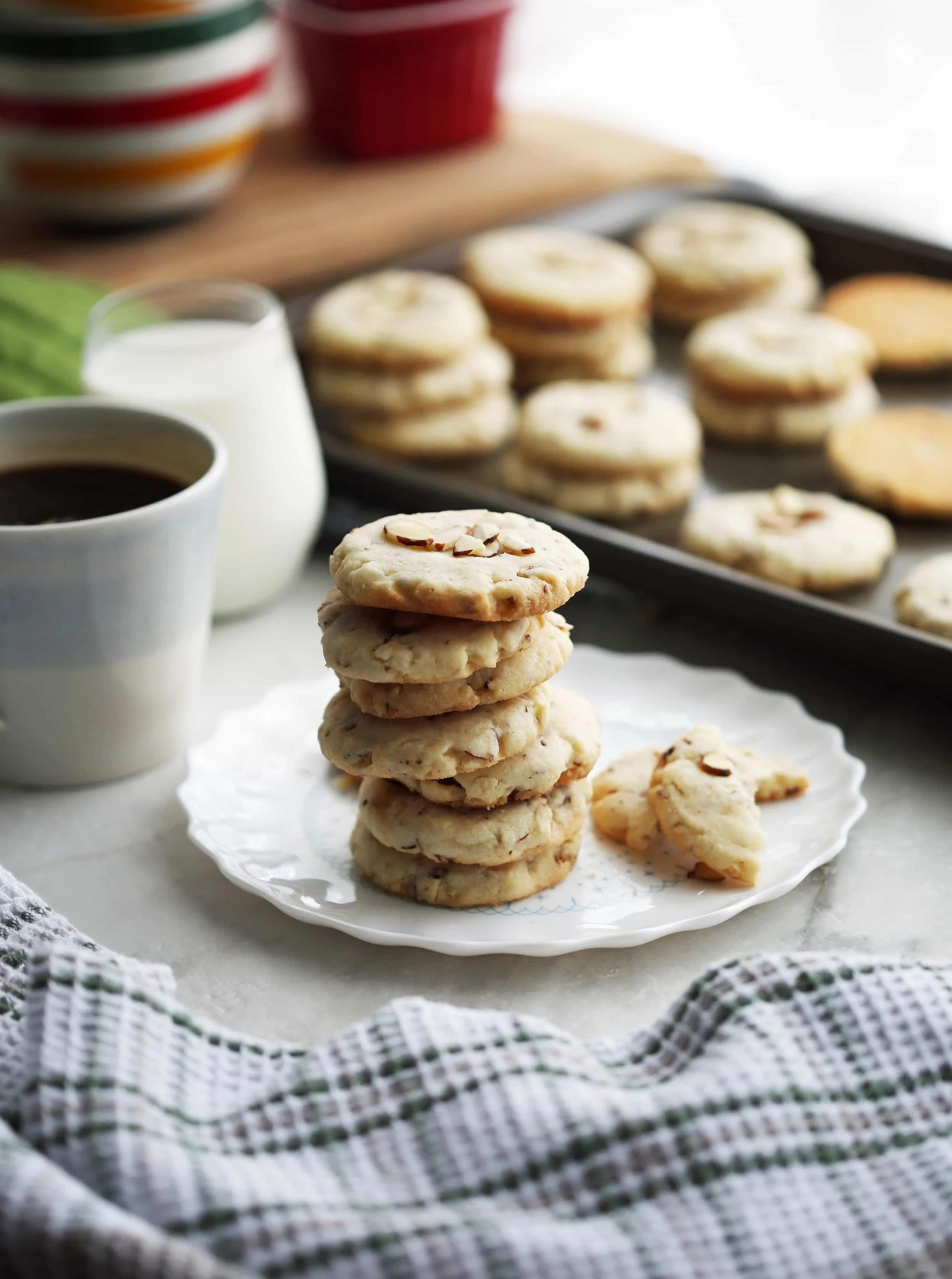 stack of almond cookies on a white plate with a cup of tea in the background
