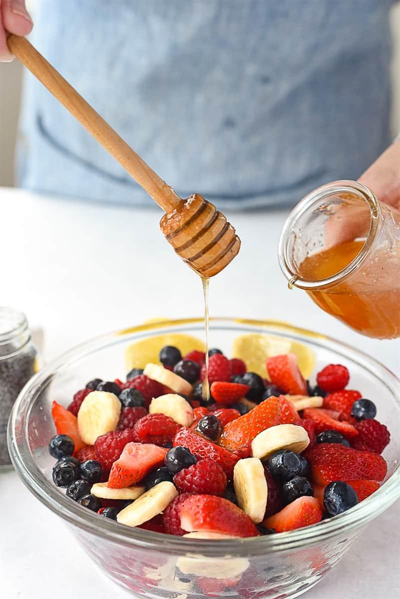 Bowl of fruit salad being drizzled with cardamom-honey dressing