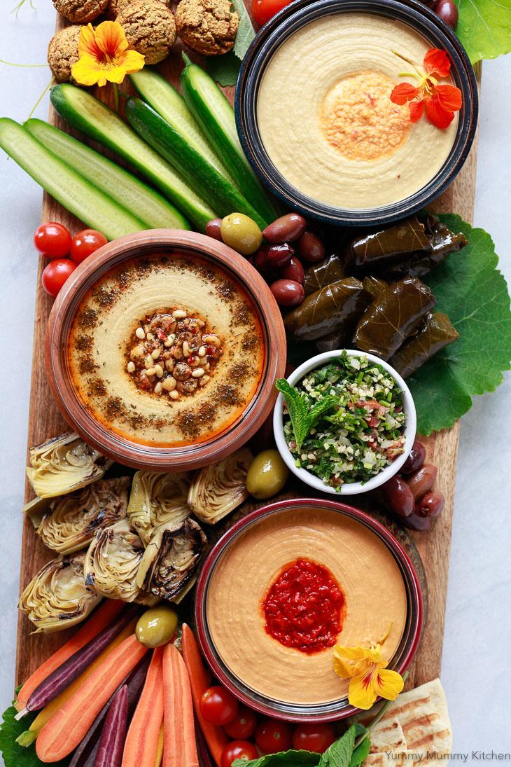 A rustic wooden table set with a plate of Mediterranean Empanadas, a bowl of hummus, and some fresh herbs