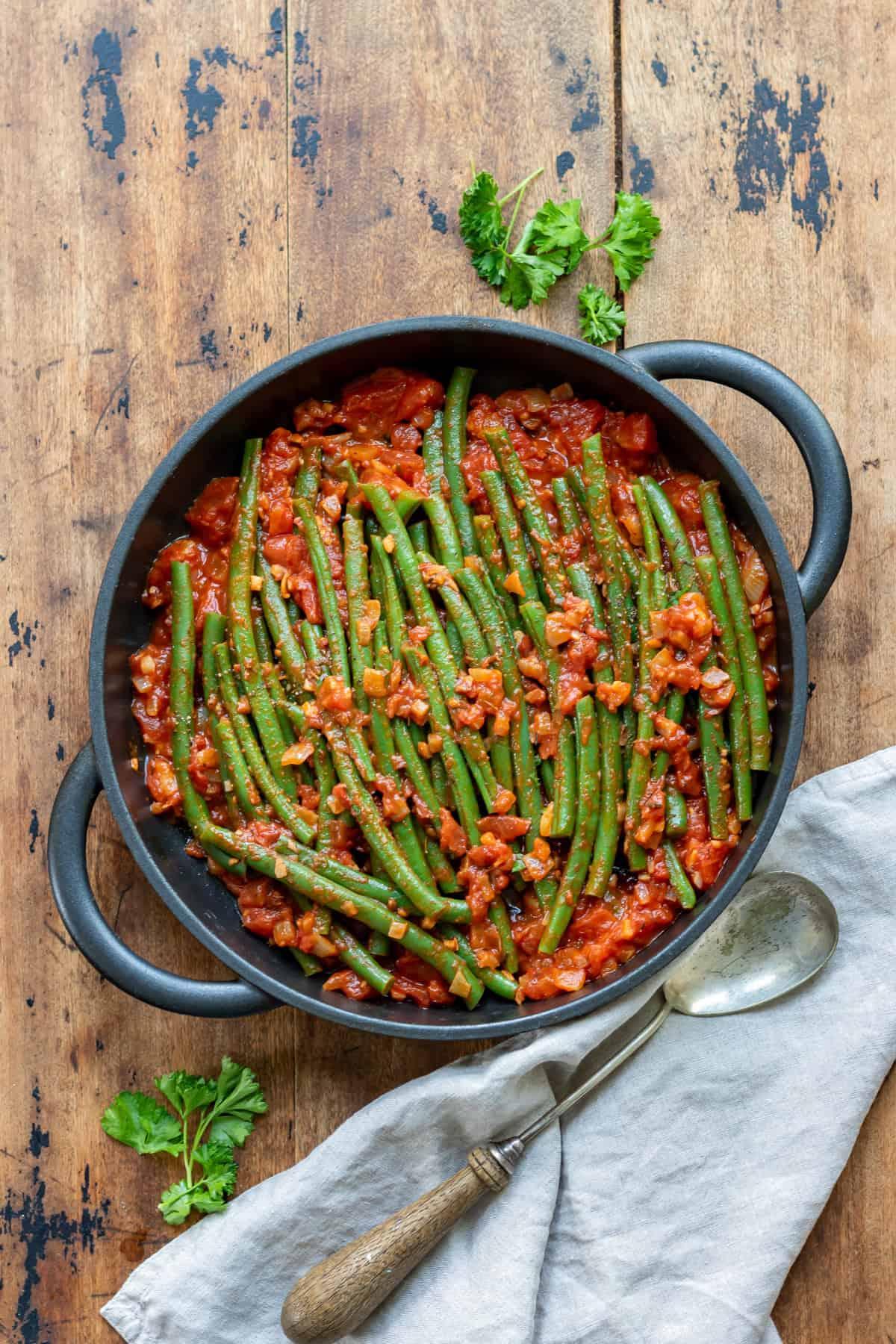 A rustic wooden table with a bowl of Rosemary and Garlic Green Beans and a serving spoon
