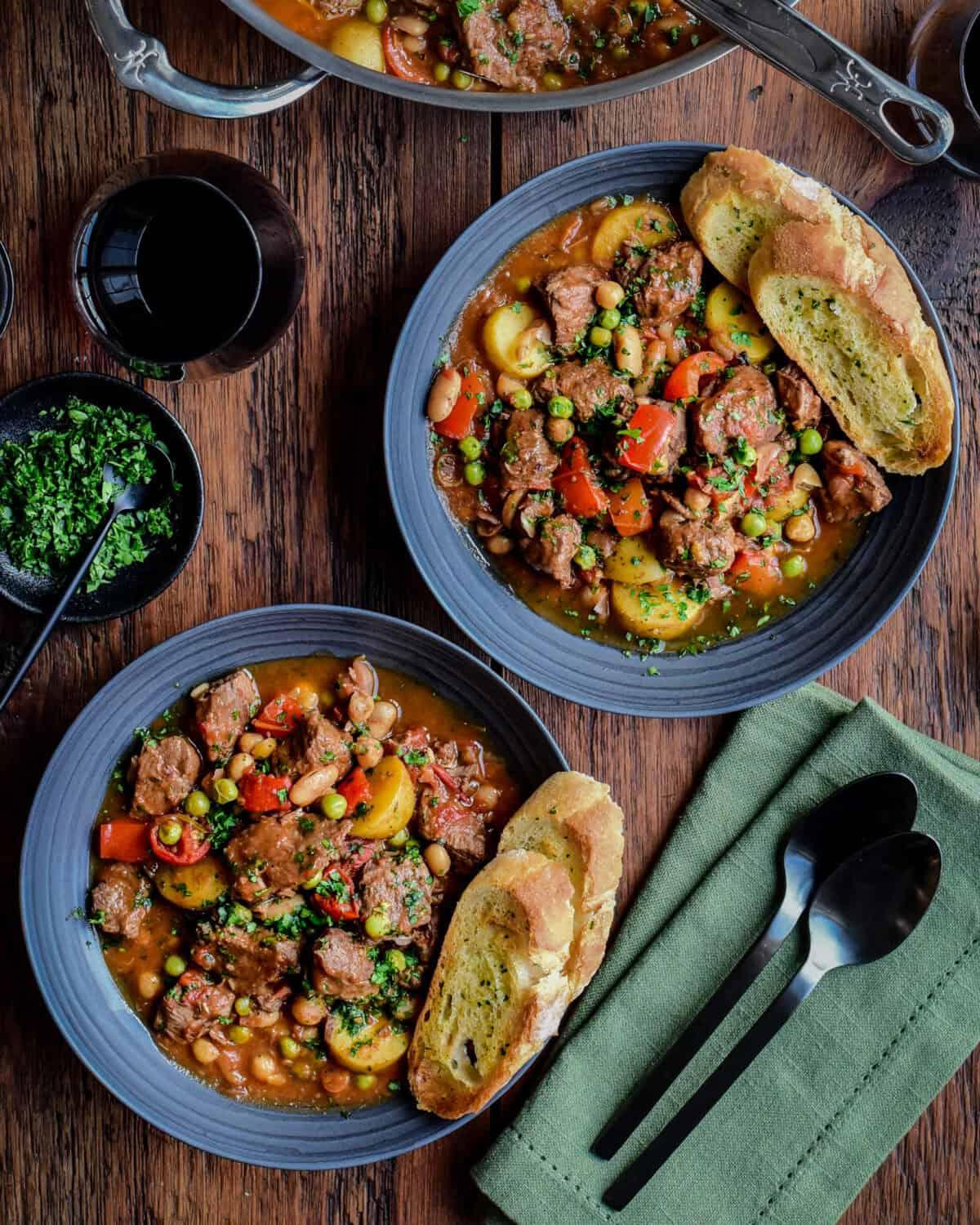 A rustic wooden table set with a bowl of Slow Cooker Mediterranean Lamb Stew and crusty bread