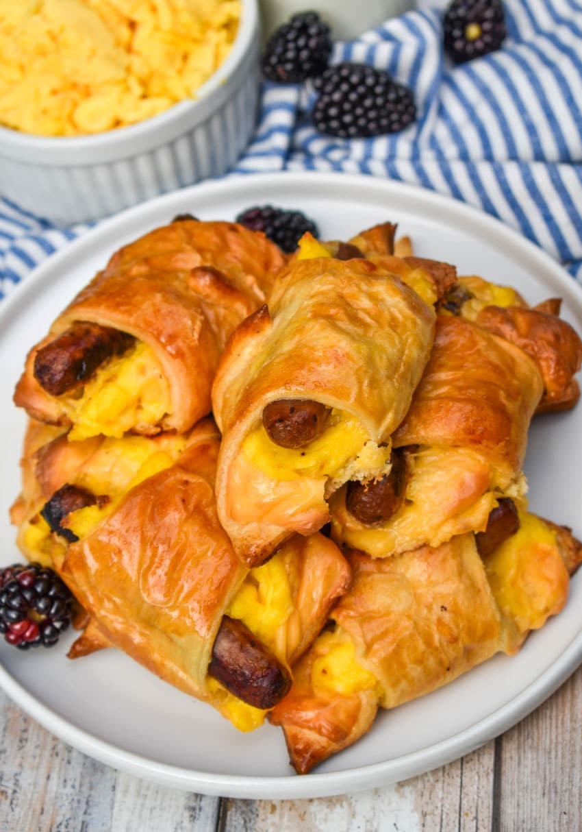 golden crescent roll ups filled with sausage and scrambled eggs on a breakfast plate