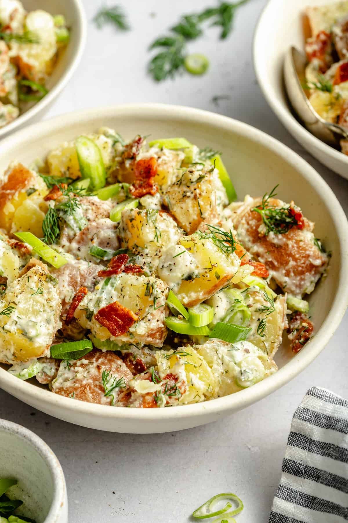 A vibrant bowl of potato salad with crispy bacon and a creamy ranch dressing, garnished with fresh parsley.