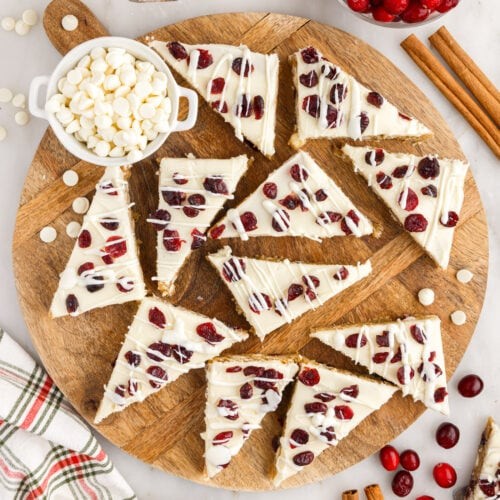 Festive cranberry bliss bars with white icing and dried cranberries on a wooden board